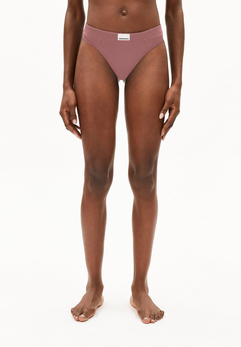 Vrouwelijk model staat blootsvoets in mauve hoge onderbroek met een wit merkje op de tailleband, tegen een witte achtergrond.