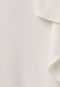 Tissu blanc lisse avec un pli doux et une couture soignée le long du bord, montrant la texture et les détails du matériau.