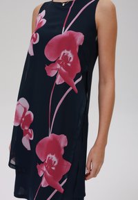 Navy-Kleid mit pinkfarbener Orchideenblütenmuster, ärmelloses Design, glatte Textur und Seitenschlitze. Leichter Stoff fällt elegant.