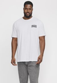 Biely bavlnený tričko s krátkymi rukávmi, na ľavej hrudi s čiernym logom "JACK & JONES". Voľný strih, hladká textúra.