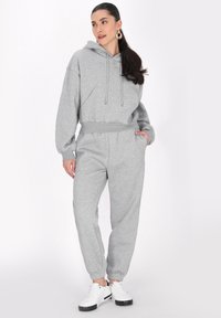 Felpa grigia con cappuccio e pantaloni abbinati realizzati in materiale morbido, caratterizzati da una vestibilità comoda, polsini elasticizzati e tasche. Abbinati a sneakers bianche.