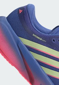 Μπλε και πράσινο παπούτσι για τρέξιμο Adidas Supernova Rise 3 με ροζ λεπτομέρειες και υφασμένο πέλμα, δείχνοντας πλευρικές και πίσω λεπτομέρειες.