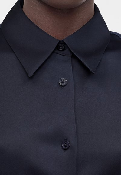 Κοντινό πλάνο για το γιακά και τα κουμπιά ενός σκούρου ναυτικού μπλε πουκαμίσου σε άτομο με σκούρο δέρμα.