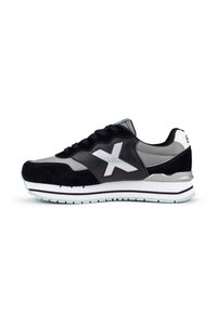 Zapatilla negra y gris con paneles de ante y cuero, con un acento blanco, cierre con cordones y una suela texturizada con una raya de menta.