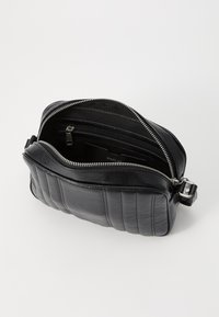 Bustina in pelle nera con texture trapuntata, chiusura con zip e tasche interne. Forma rettangolare compatta con dettagli in metallo argentato.