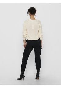 Krämfärgad stickad tröja med ribbade ärmar, tillsammans med svarta cargo-byxor som har sidofickor och åtsittande anklar, kompletterat med svarta högklackade stövlar.