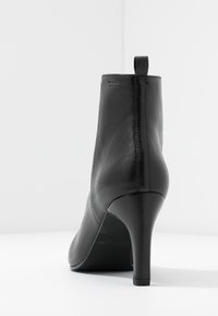 Botas de cuero negras hasta el tobillo con un diseño elegante, puntera puntiaguda y un tacón alto y estrecho. Incluyen una pestaña trasera para facilitar su uso. Textura suave.