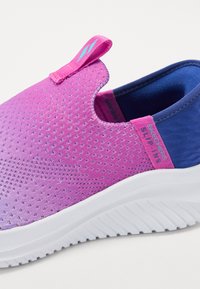 Lila hálós slip-on cipő textúrált felsővel, kék részletekkel, fehér talppal és rózsaszín hurkokkal a könnyű felvétel érdekében. Légáteresztő anyaggal készül.