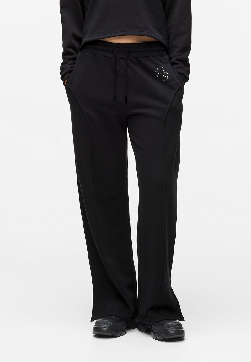 Pantaloni de trening negri cu talie elastică, buzunare laterale și accente decorative din strasuri pe șold. Confecționați dintr-un material moale, cu o croială lejeră.