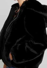 Zwarte nepbontjas met een capuchon, voorzien van een ritssluiting, zachte textuur en zijzakken, ontworpen voor warmte en comfort.