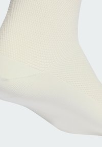 Biała skarpetka za kostkę z teksturowanym wzorem siateczkowym i prążkowanym mankietem. Materiał wydaje się gładki z oddychającym designem, idealnym dla komfortu.