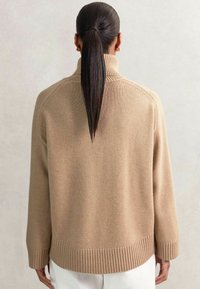 Beige coltrui met geribde afwerking aan de onderkant en mouwen, gemaakt van zachte, textuurstof. Heeft een relaxte pasvorm en een verlaagde schouderlijn.