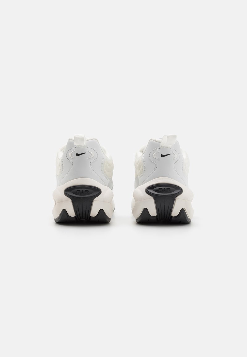 Białe i kremowe sneakersy Nike z teksturowanymi materiałami, zaokrąglonym kształtem, czarną podeszwą oraz detalem logo na pięcie, z uchwytem.