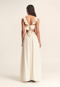 Vestido maxi en marfil con lunares negros; cuenta con mangas rizadas, espalda abierta con detalle de lazo y falda fluida; hecho de una tela ligera.