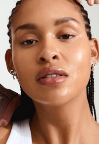 Silver hoop earrings featuring a bow design, smooth texture, and polished finish, worn by a person with braided hair and minimal makeup.