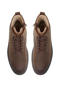 Botas de tobillo de cuero marrón con ojales dorados, cordones redondos y un interior forrado de pelo. Cuentan con cremalleras laterales y suelas de goma para mayor tracción.