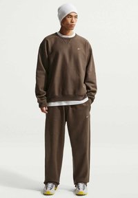 Sweat-shirt marron et pantalon assorti en tissu doux. Bonnet blanc, baskets grises avec des accents jaunes. Logo Nike sur la poitrine et le pantalon.