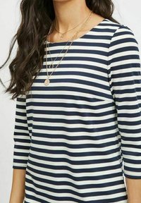 Námořnické a bílé pruhované tričko s dlouhým rukávem a kulatým výstřihem; obsahuje vrstvené zlaté náhrdelníky; materiál vypadá měkký s mírným elastickým tahem.