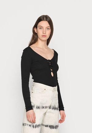 T-shirt preto de manga longa com um decote em V profundo e um laço no centro, combinado com calças brancas de cintura alta com um padrão de tie-dye preto.