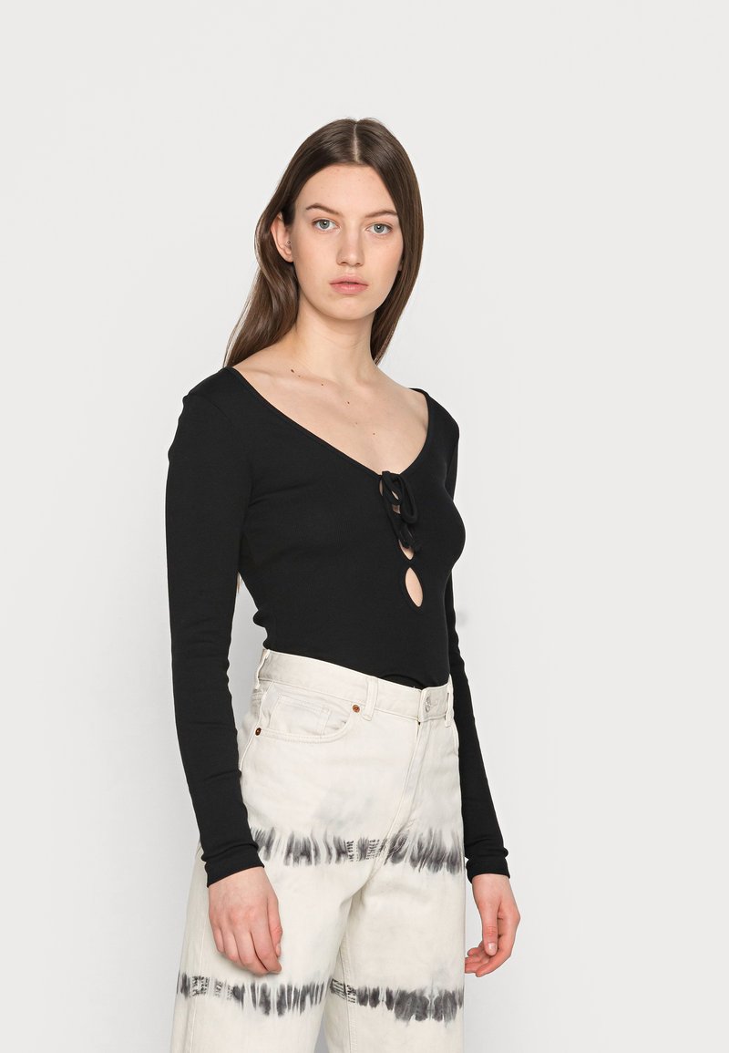 T-shirt preto de manga longa com um decote em V profundo e um laço no centro, combinado com calças brancas de cintura alta com um padrão de tie-dye preto.