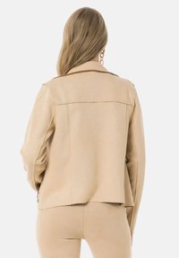 Veste en suédine beige avec un design ajusté, col cranté et épaulettes. Comprend une poche latérale zippée et une coupe décontractée.