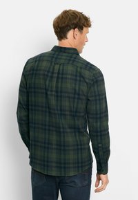 Grüne und marineblaue karierte Bluse mit langen Ärmeln, Button-Down-Kragen und abgerundetem Saum; verfügt über einen einzelnen Rückenfalten und Knopfmanschetten.