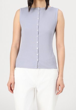 Bezrękawnik, jasnofioletowy prążkowany top z zapięciem na guziki z przodu, o subtelnej fakturze i dopasowanym kroju. Zestawiony z białymi spodniami.