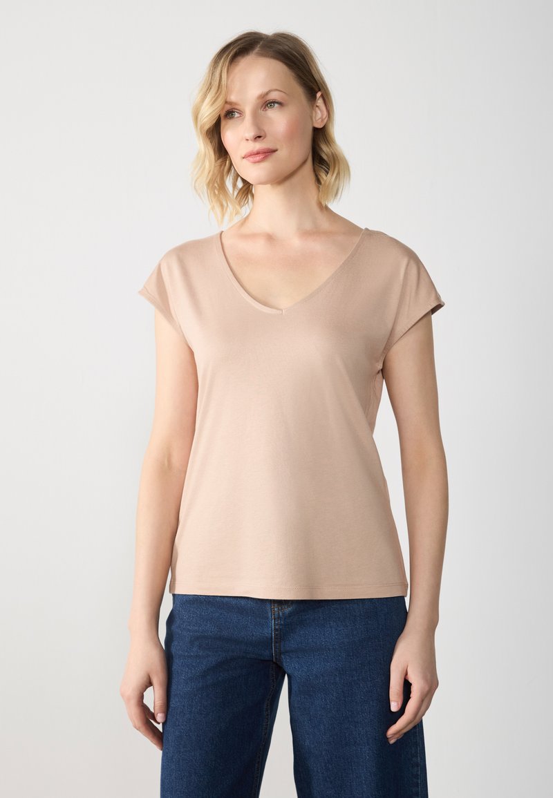 Kortærmet T-shirt med v-hals i blød beige stof. Skarpe kanter, afslappet pasform, minimalistisk design med glat tekstur, parret med blå jeans.