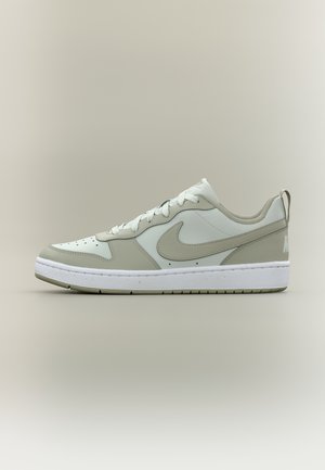 Baskets basses blanches et gris clair avec lacets, bout perforé, logo Nike swoosh, et semelle blanche épaisse sur fond uni.