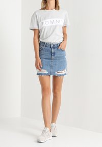 Grå t-shirt med vitt "TOMMY"-tryck, sliten denimkjol, vita sneakers. Avslappnad outfit med minimala detaljer, enkel design och avslappnad passform.
