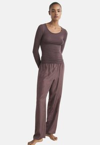 Top burdeos de manga larga con escote redondeado, combinado con pantalones sueltos a juego. Ambas prendas tienen una textura suave y un ajuste relajado.