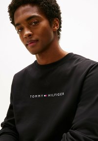 Felpa nera con collo a girocollo e logo ricamato "TOMMY HILFIGER" in bianco con accenti rossi e blu. Tessuto morbido.