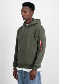 Felpa verde oliva, tessuto misto cotone, tasca a marsupio, polsini e orlo a coste, con logo dorato e zip rossa con dettagli testuali.