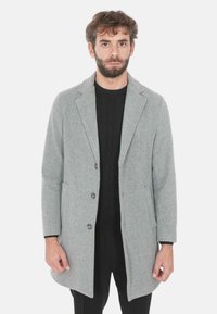 Cappotto in lana grigio con colletto a punta, due tasche frontali e tre bottoni. Presenta una vestibilità su misura e una superficie liscia.