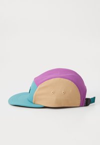 Căciulă colorată cu față teal, vârf violet și spate bej. Prezintă o margine plată, material texturat și o curea ajustabilă în spate.