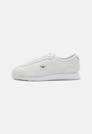 Sneaker bianco in pelle con punta rotonda, chiusura a lacci e design classico. Presenta un logo argentato e suola in gomma testurizzata.