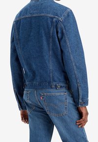 Veste en denim de couleur bleu foncé, avec un motif texturé subtil, un devant à boutons, un design classique, des poches latérales et des poignets ajustables.
