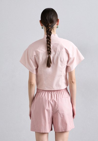 Camicia rosa leggera e corta con maniche corte abbinata a pantaloni corti a righe rosa e bianche con elastico in vita e tasca.