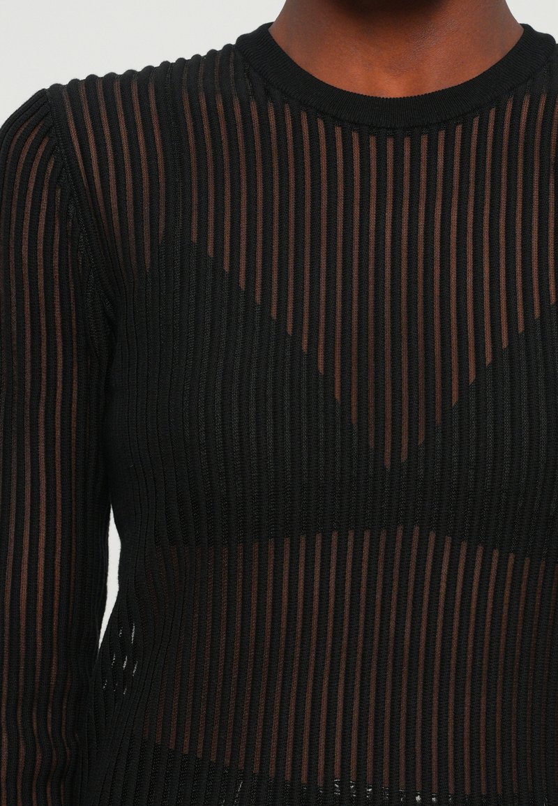Schwarzes Strickoberteil mit vertikalen Streifen, durchsichtigen Abschnitten und rundem Halsausschnitt. Das Muster besteht aus abwechselnd soliden und transparenten Bereichen.