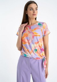 Krótki rękaw top w lekkim, purpurowym materiale z kolorowym, abstrakcyjnym wzorem. Posiada węzeł po boku dla dopasowanego wyglądu.