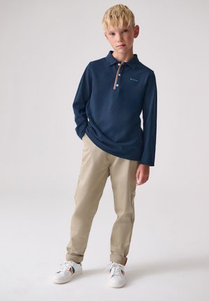 Granatowa koszulka polo z długim rękawem, trzema guzikami i pomarańczowym akcentem, połączona z beżowymi chinosami i białymi trampkami z kolorowymi detalami.