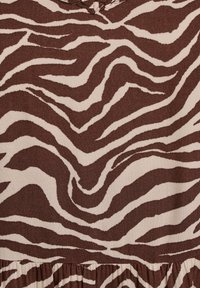 Tkanina smeđe i krem boje s uzorkom zebra pruga, teksturirana površina, s nabranim rubom na dnu.