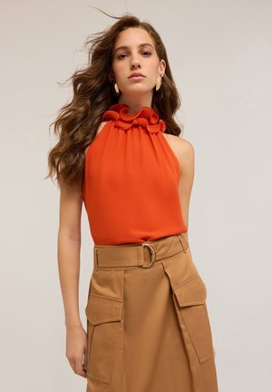 Orange sleeveless top with ruffled neckline paired with a khaki skirt featuring large pockets and a circular belt buckle. Smooth fabric texture.