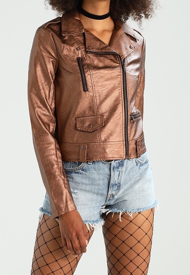 Veste moto en cuir synthétique marron métallisé avec un large col, poches zippées et une silhouette ajustée, associée à un short en denim et des collants en résille.
