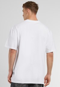White cotton t-shirt with a relaxed fit, short sleeves, and a crew neck. Features a smooth texture and side tag detail.