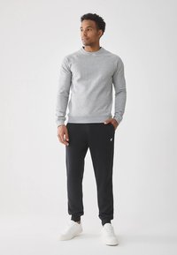 Grå hættetrøje med lange ærmer kombineret med sorte joggingbukser. Hvide sneakers fremhæver outfittet. Minimalistisk design og glatte teksturer.