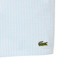 Tela a rayas en azul claro y blanco con un acabado texturizado; presenta un logo de cocodrilo bordado en verde en la esquina inferior izquierda.