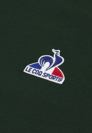 Tissu vert avec une texture douce comportant un logo brodé : un escargot bleu sur une forme blanche, agrémenté de détails rouges et bleus.