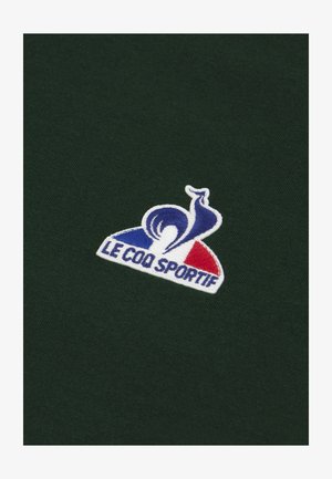 Groene stof met een zachte textuur, voorzien van een geborduurd logo: een blauwe slak boven een witte vorm, accentueert met rode en blauwe details.