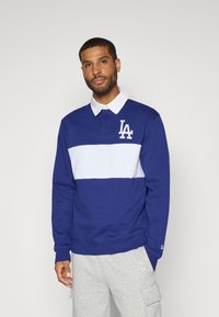 Mørkeblå sweatshirt med hvid stribe og broderet "LA"-logo. Har krave og ribbede manchetter, lavet af blødt, tekstureret stof.